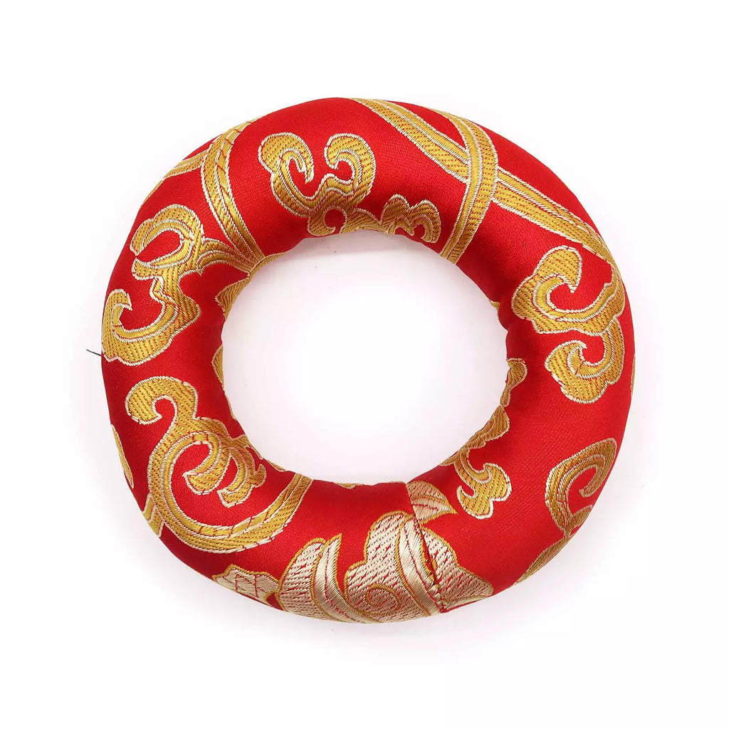 A red fabric ring cushion with ornate gold embroidered patterns, photographed on a clean white background.