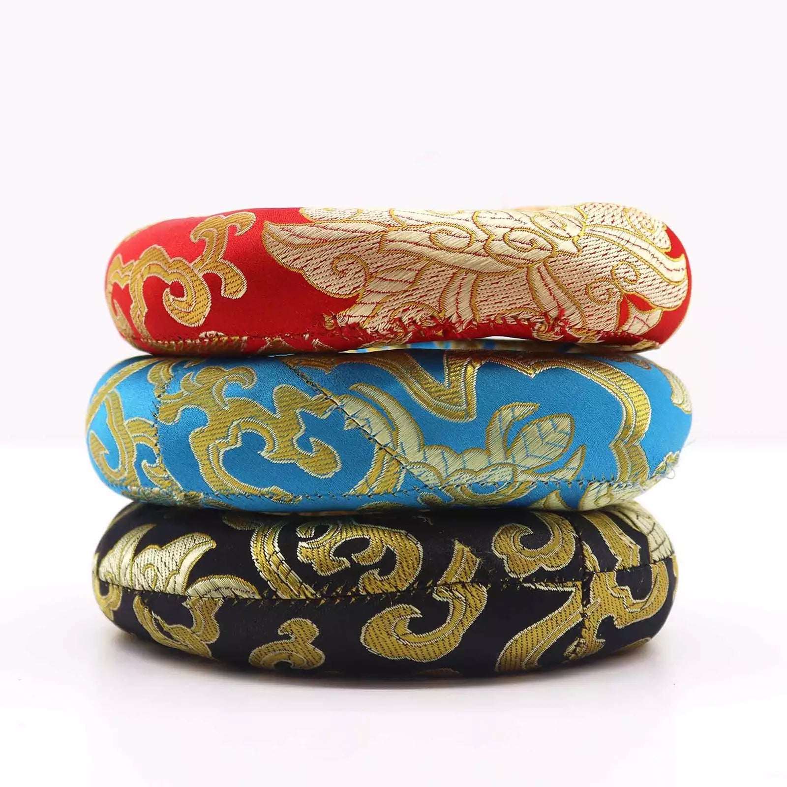 Three stacked circular fabric pouches or covers in red, blue, and black, each decorated with ornate gold brocade-style patterns on a white background.