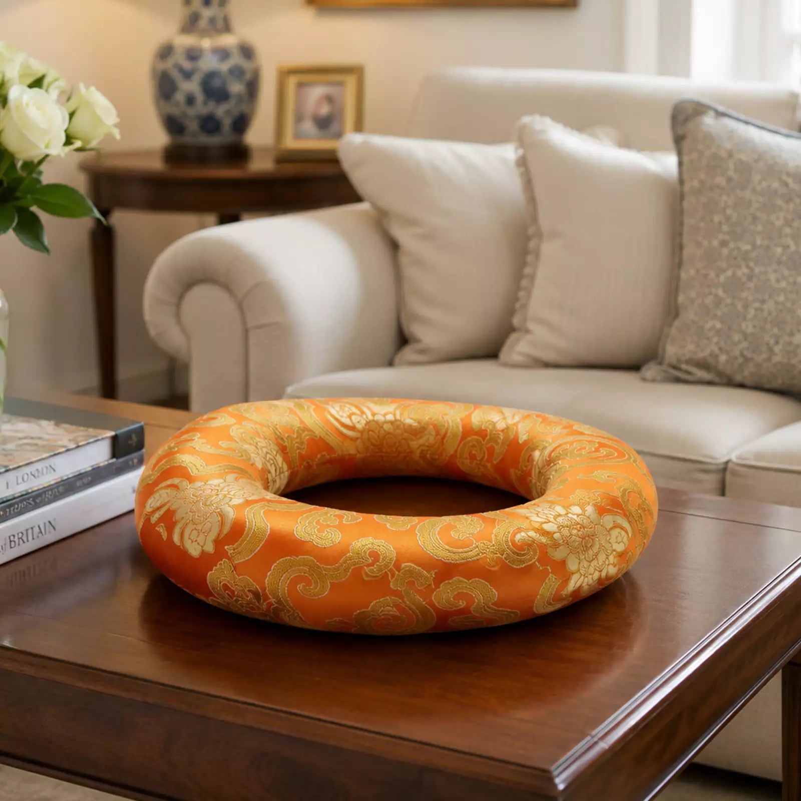 An orange and gold patterned circular cushion or ring-shaped pillow displayed on a dark wooden coffee table in a living room setting.