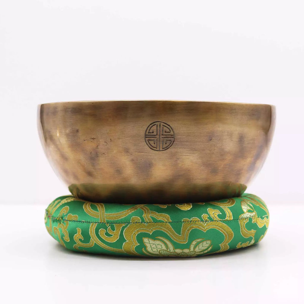 Bronze singing bowl with a green cushion on a white background