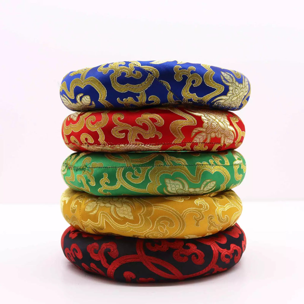 A stack of five round cushion covers or small ottomans made of ornate brocade fabric, shown on a plain light background. The colors from top to bottom are blue, red, green, yellow, and black, each with a gold cloud-like pattern.