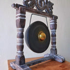 Traditional gong on a wooden stand against a plain wall
