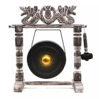 A decorative hanging gong set on a weathered wooden stand with ornate dragon-like carvings at the top, a black gong with a gold center, and a hanging mallet on a white background.