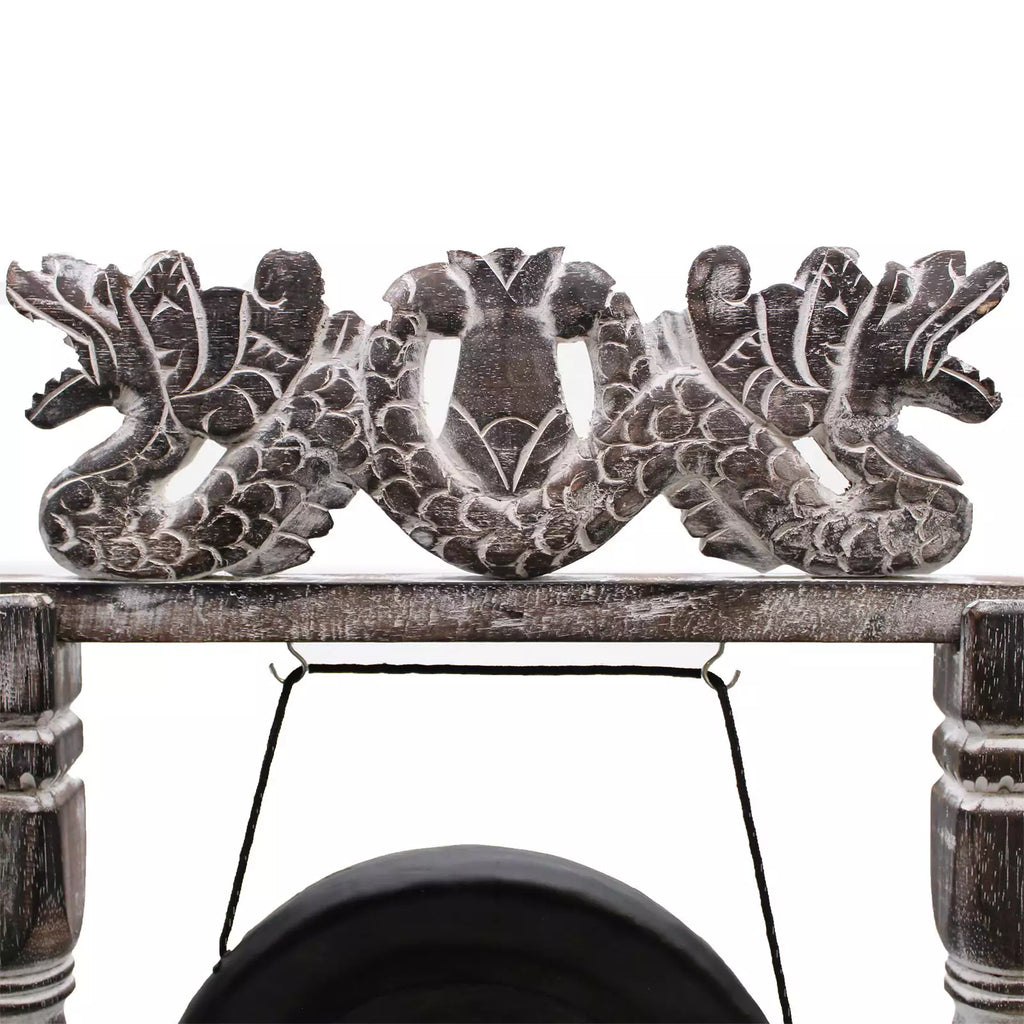 A close-up of a carved wooden decorative piece featuring two dragon figures flanking a central motif, mounted on a rustic wooden beam with a hanging black cord below.