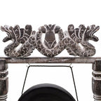 A close-up of a carved wooden decorative piece featuring two dragon figures flanking a central motif, mounted on a rustic wooden beam with a hanging black cord below.