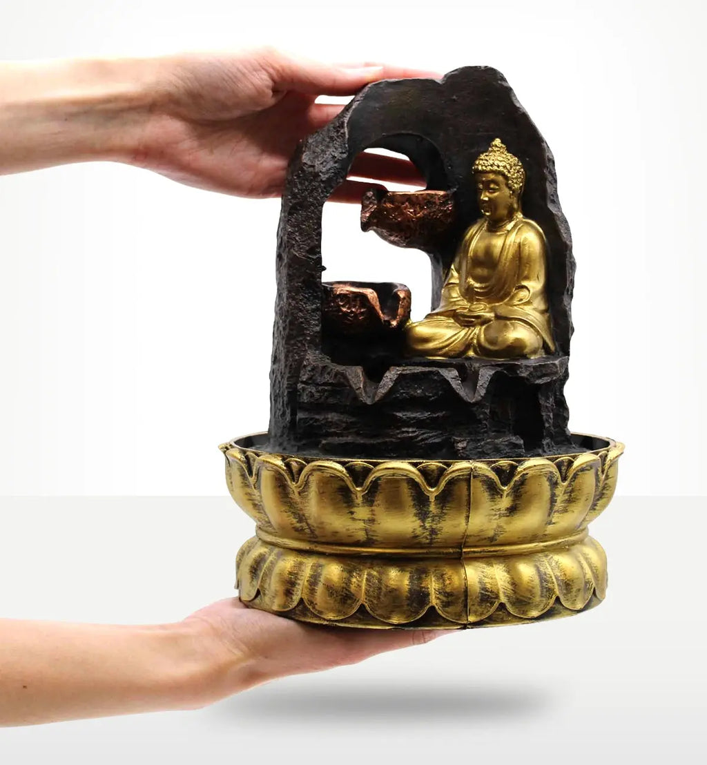 Hands holding a Tabletop Water Feature - 30cm - Golden Meditating Buddha with a carved resin Buddha statue seated inside a stone-like frame above a decorative golden base.
