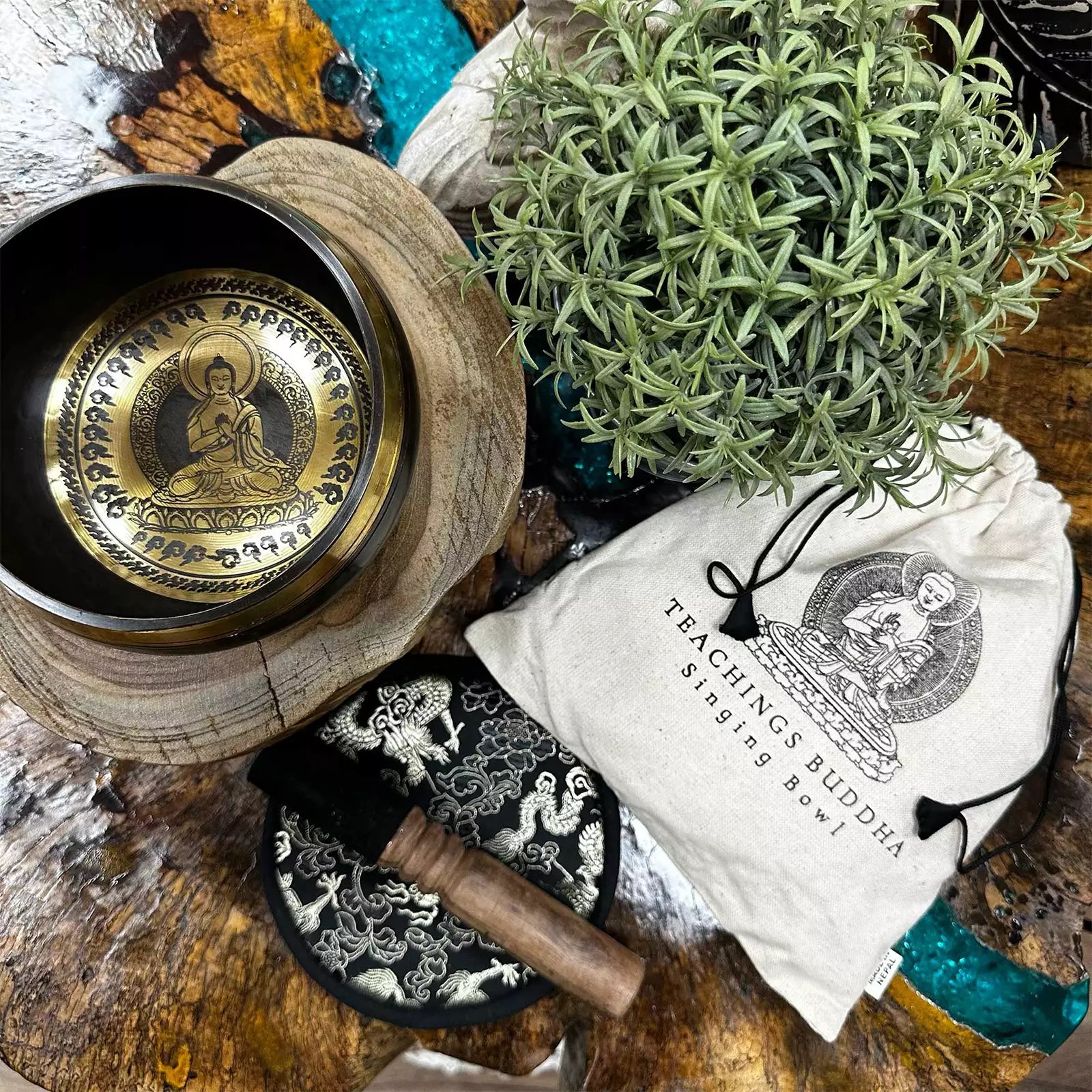 Buddhist singing bowl set with wooden mallet, pouch, and decorative elements on a wooden surface.