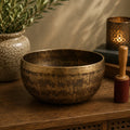 Tibetan Healing Engraved Bowl - 16cm - Mantra with intricate golden script patterns, placed on a wooden surface alongside a mallet, ceramic vase, and lit candle creating a peaceful ambiance.