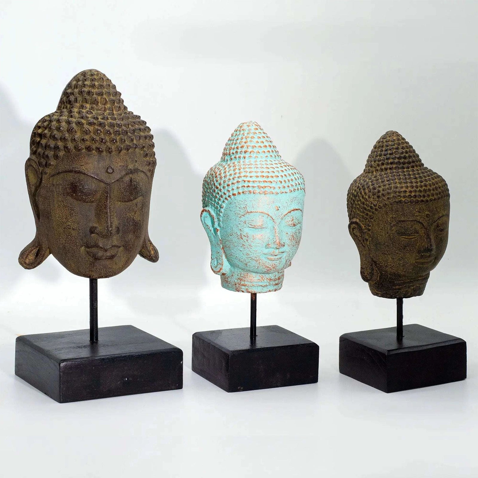 Three Buddha head sculptures on stands against a white background