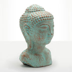 A decorative Buddha head bust sculpture with a distressed turquoise and rust-colored patina, set against a plain white studio background.