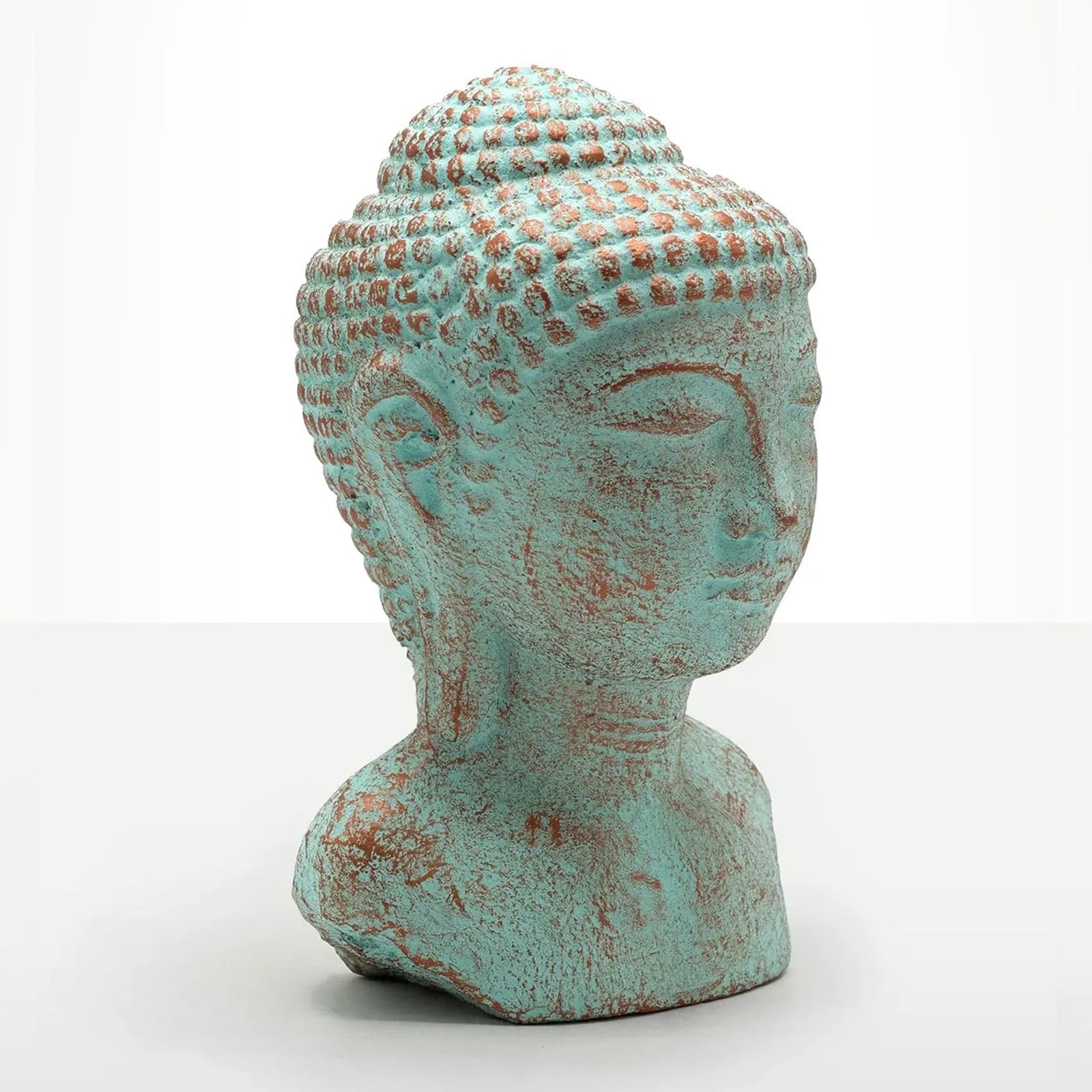 A decorative Buddha head bust sculpture with a distressed turquoise and rust-colored patina, set against a plain white studio background.