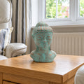 Green copper Buddha head on an oak side table beside a bay window in a British sitting room.