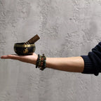 Hand holding a small black bowl with a wooden tool against a gray textured wall
