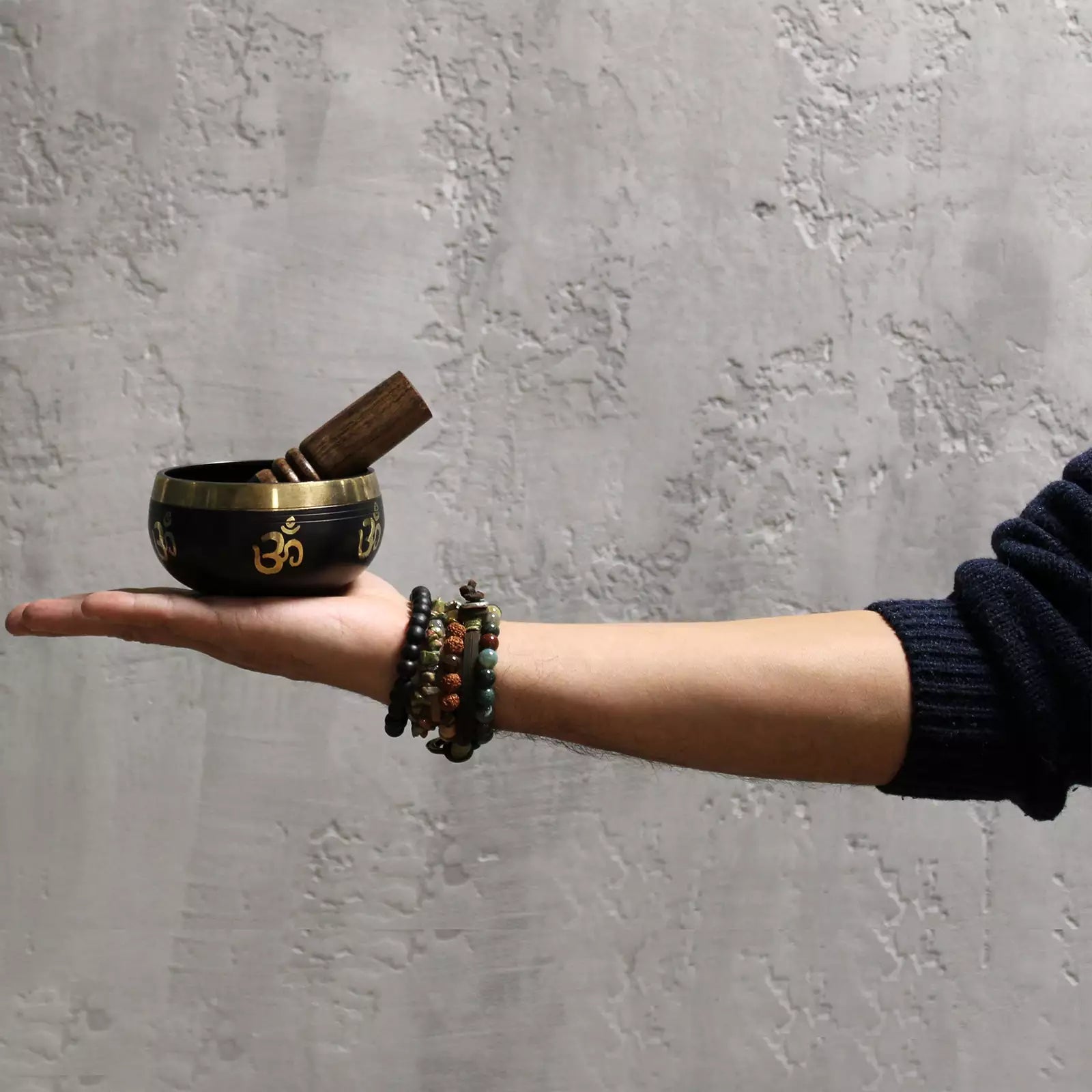 Hand holding a small black bowl with a wooden tool against a gray textured wall