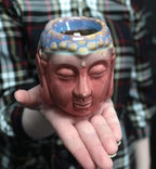 Person holding a hand-crafted Buddha Oil Burner - Rose & Teal, featuring a serene Buddha face with rose-colored base and teal accents on top, perfect for Buddha decor and relaxation.