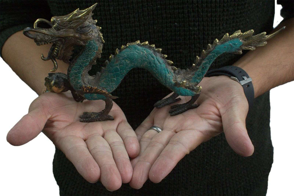 A person holding a detailed Fengshui - Med Dragon with Ball - 27cm sculpture featuring green and bronze tones, showcasing intricate scales and features.