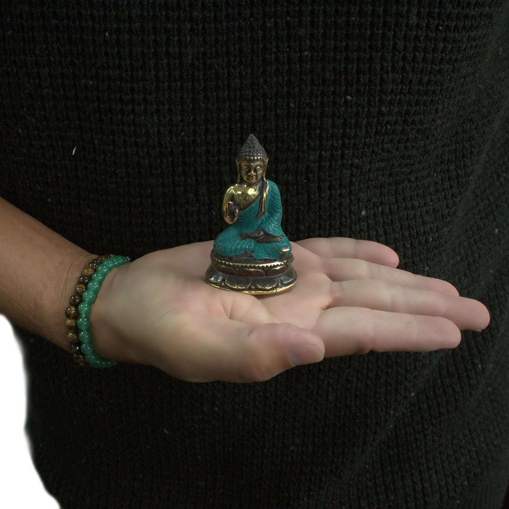 A person wearing a dark sweater holds a Mini Hand Up Sitting Buddha statue with turquoise and gold coloring in their open palm, showcasing the small size and intricate details.