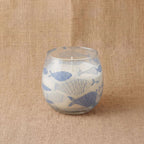 Small Glass Jar Candles - Seabreeze featuring a white candle in a clear glass jar decorated with blue fish illustrations, set on a textured beige fabric background.