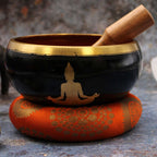 Large Buddha Singing Bowl Set- Black/Orange 14cm featuring a black bowl with a golden Buddha silhouette, resting on an ornate orange cushion with a wooden striker.