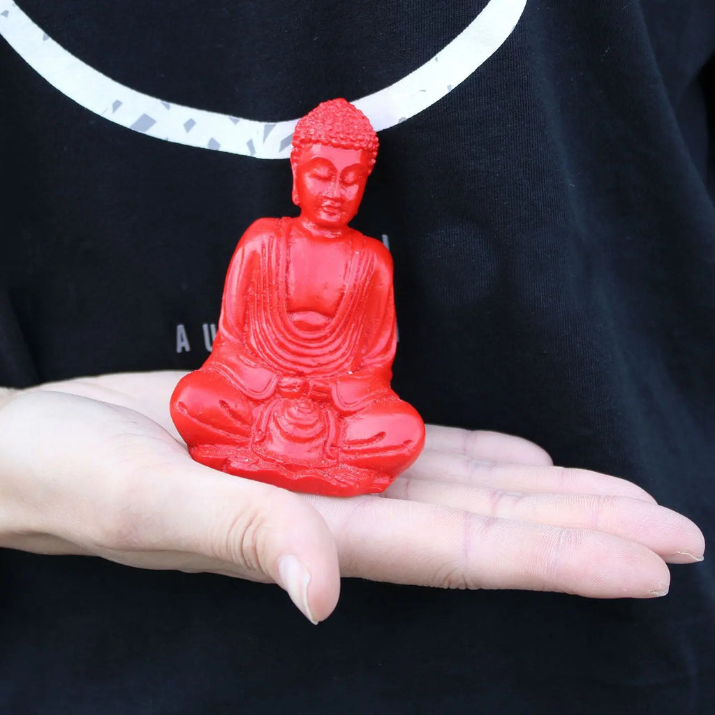Person holding a vibrant red Matt Mini Buddha (Assorted Colours) statue in their palm, showcasing a small, detailed Buddha decor piece ideal for tabletop display.