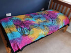 Single Cotton Bedspread + Wall Hanging - Peaceful Buddha featuring a vibrant multicolor tie-dye background with an intricate black outline of a meditating Buddha and lotus petals, displayed on a wooden bed frame.