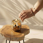 Hand lighting a Small Glass Jar Candles - Amber Mosaic with a match on a wooden table in soft natural light