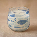 Medium Glass Jar Candles - Seabreeze featuring a clear glass jar decorated with blue fish illustrations on a natural textured surface.