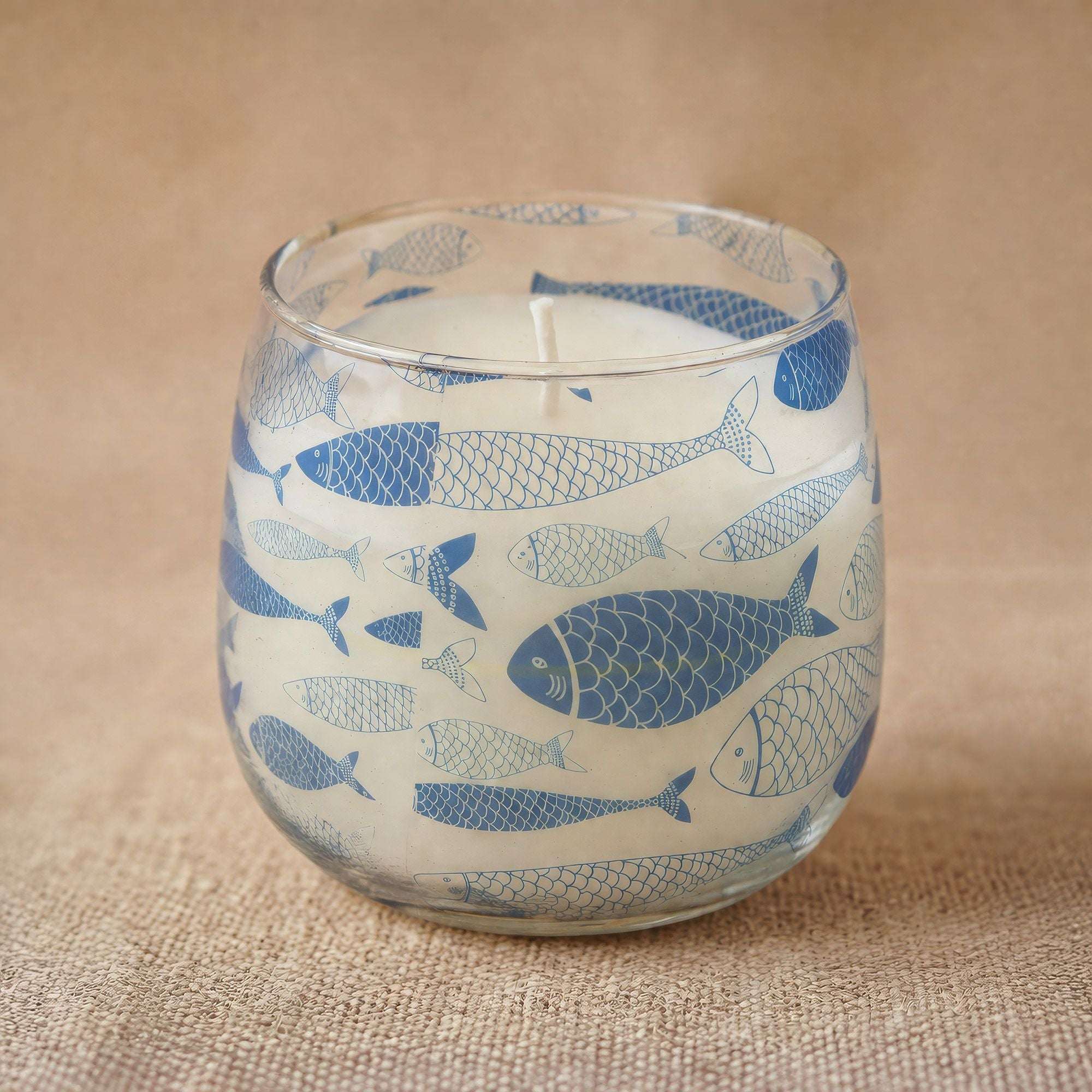 Medium Glass Jar Candles - Seabreeze featuring a clear glass jar decorated with blue fish illustrations on a natural textured surface.