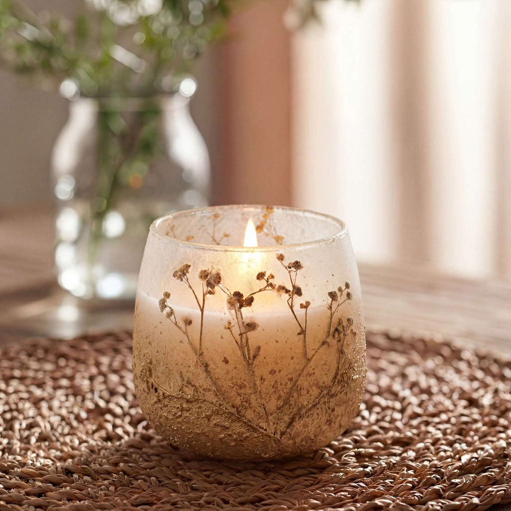 Medium Glass Jar Candles - Wildlight Woods with delicate dried floral accents inside a frosted glass jar, softly glowing on a woven surface in a cozy, natural setting.
