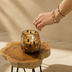Hand lighting a Medium Glass Jar Candles - Amber Mosaic with a match on a natural wooden table in soft natural light.