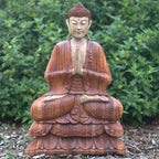 Hand Carved Buddha Statue - 80cm Welcome sitting in meditation with hands in prayer position, crafted in warm-toned wood, displayed outdoors with green foliage background.