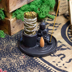 Multi Purpose Buddha Incense Plate - Ceramic Matt Black featuring a seated Buddha statue, with compartments holding incense sticks, cones, and a bundle of sage, set on a patterned cloth.