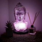 Buddha Bust Lamp Lavender Crackle - Oval Stand glowing softly in lavender light, placed on a woven mat beside a plant and reed diffuser, creating a serene ambiance.