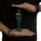 Med Standing Buddha statue in green and gold tones held between two hands wearing bracelets and a watch, showcasing the compact size and intricate hand carving details.