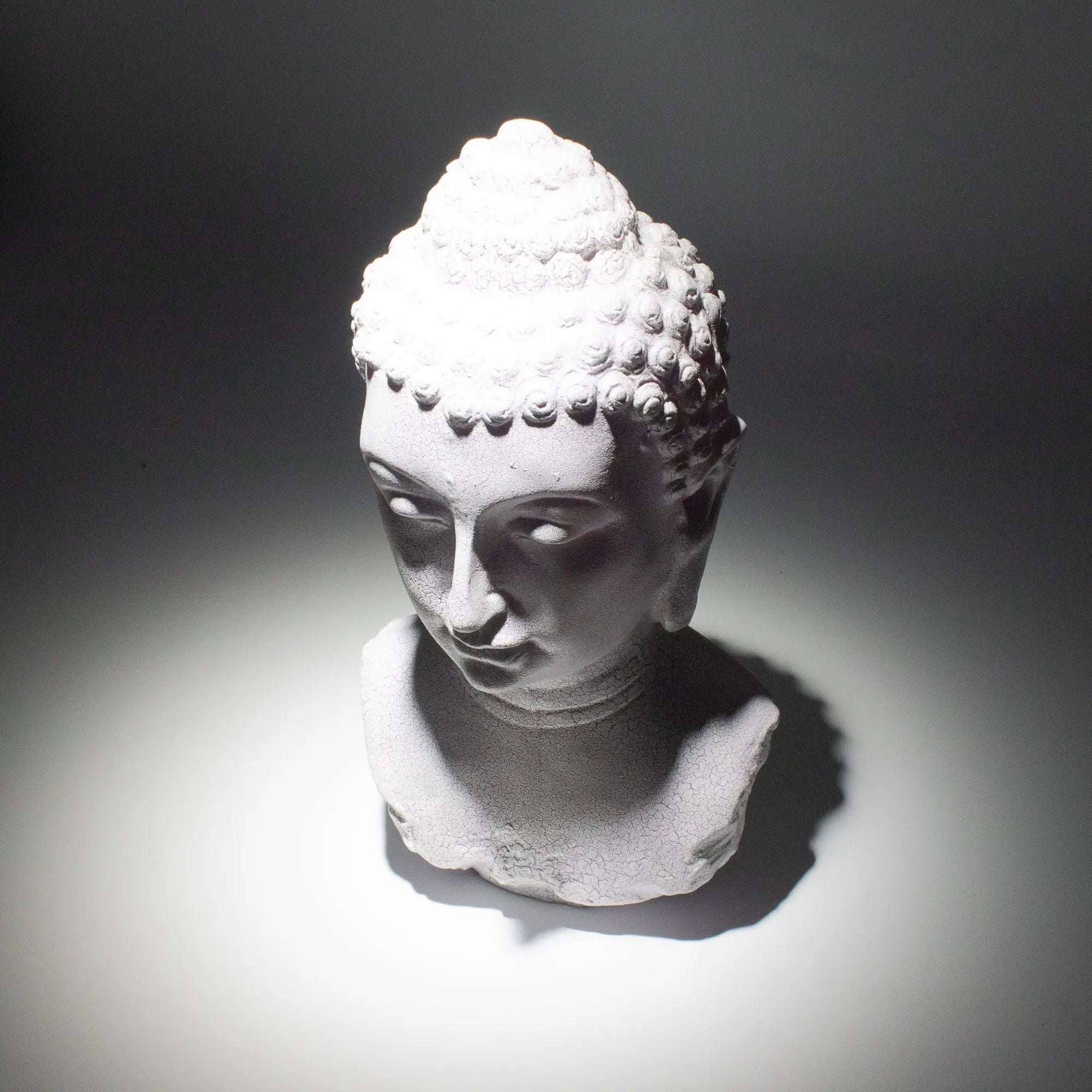 White Buddha bust statue illuminated by a soft spotlight on a dark background, showcasing intricate curls and serene facial features, Buddha Bust Lamp Lavender Crackle - Oval Stand.