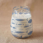 Tall Glass Jar Candles - Seabreeze featuring a clear glass container decorated with blue fish patterns, filled with white wax on a natural fabric surface.