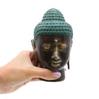 Hand holding a Large Antique Brass Buddha Head with a serene expression, featuring detailed textured hair and subtle golden highlights on the face.