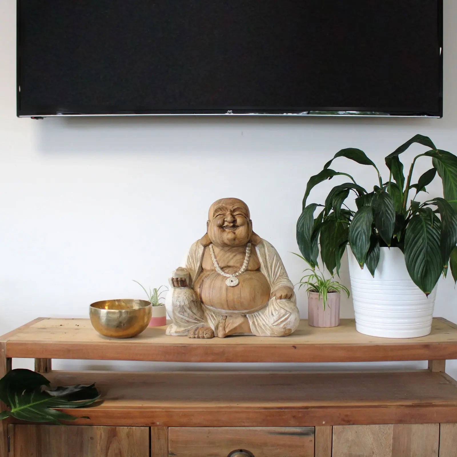 Happy Buddha - Whitewash 40cm statue displayed on a wooden shelf between two potted plants with a brass bowl, creating a serene Buddha decor centerpiece.