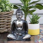 Black & Grey Buddha - Medium handcrafted resin statue sitting in meditation pose with detailed robe and serene expression, surrounded by green potted plants on rustic wooden surface.