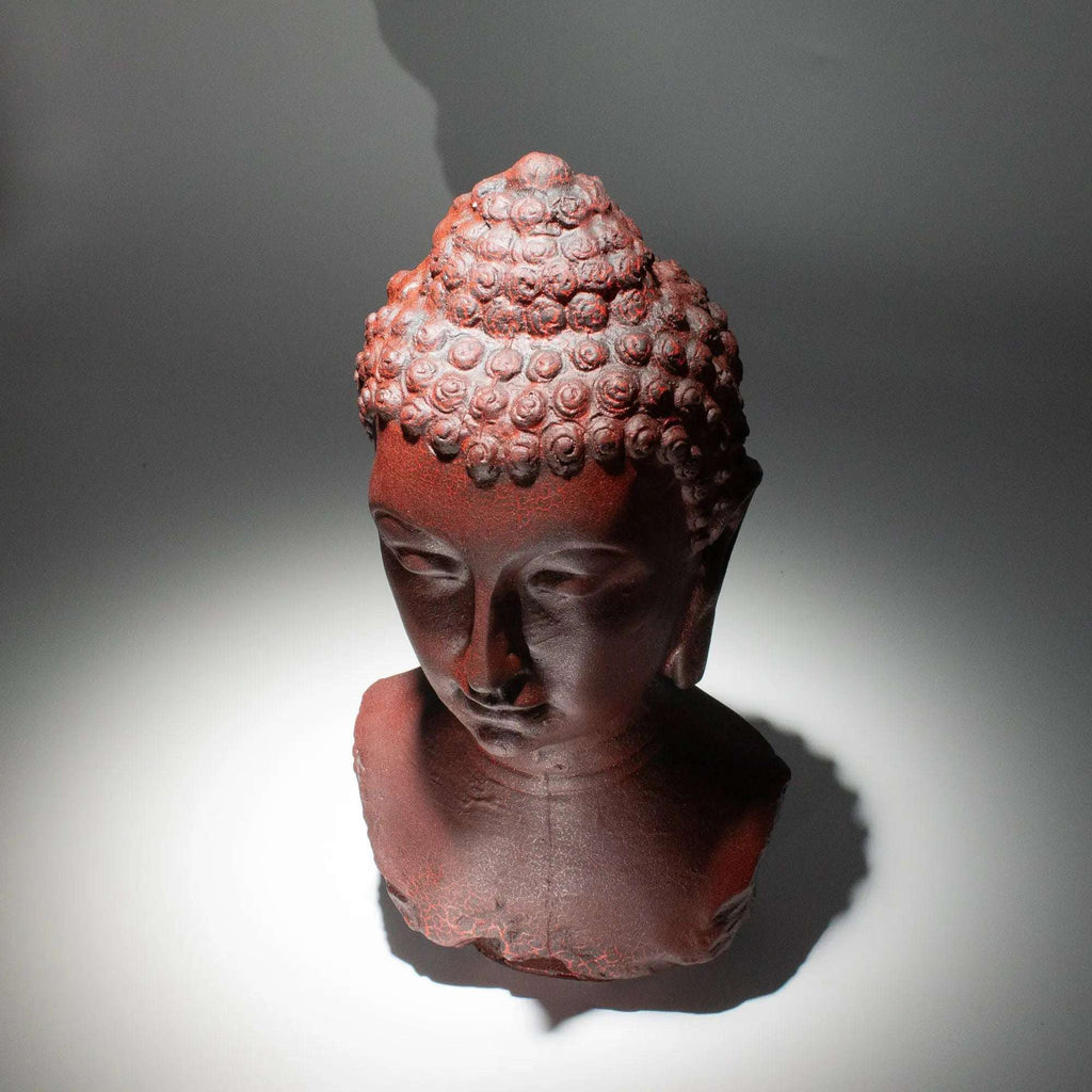 Buddha Bust Lamp Molton Lava - Oval stand featuring a textured Buddha head sculpture with a dark reddish lava-like finish, casting a serene shadow on a grey background.