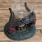 Antique Buddha - Offering Hands Oil Burner featuring intricately detailed hands in a dark finish holding a clear glass bowl, set on a textured base with red and gold accents.