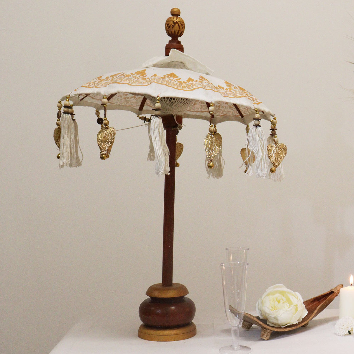 Decorative Bali Home Decor Parasol - Canvas - Gold Decor- 40cm with intricate gold patterns and hanging tassels, displayed on a wooden stand next to candles and glassware.