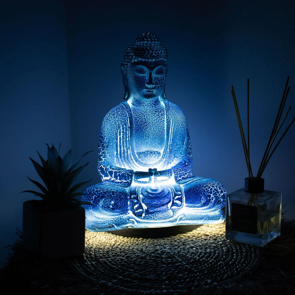 Meditation Buddha Lamp Sky Blue - Oval Stand glowing softly with a serene blue light, placed on a woven mat beside a plant and reed diffuser for calming home decor.
