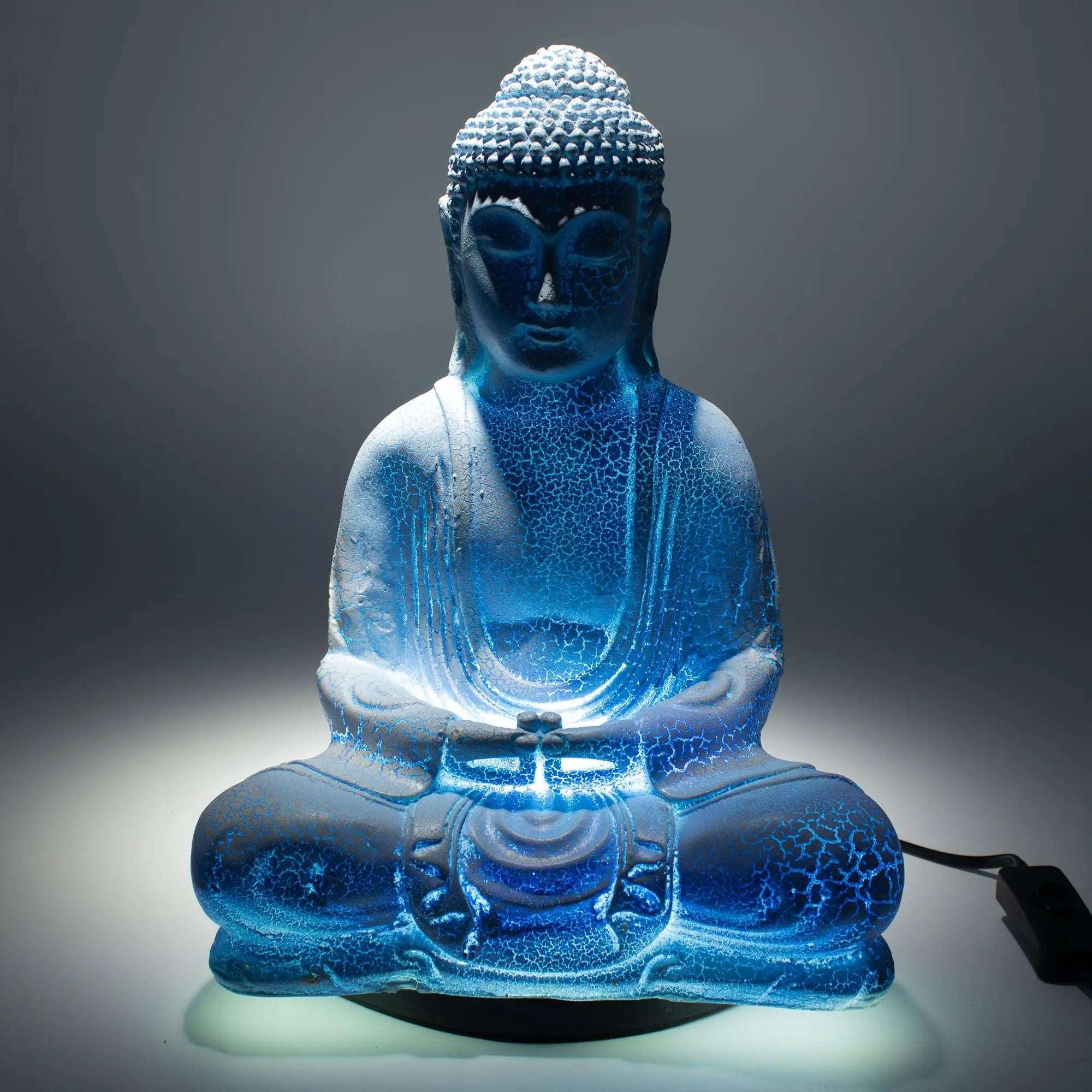 Meditation Buddha Lamp Sky Blue - Oval Stand showcases a serene blue Buddha glow lamp with cracked resin texture, seated in meditation pose on an elegant oval base.