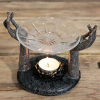 Antique Buddha - Om Hands Oil Burner with handcrafted metal hands holding a decorative glass dish above a lit tealight candle on a rustic wooden surface