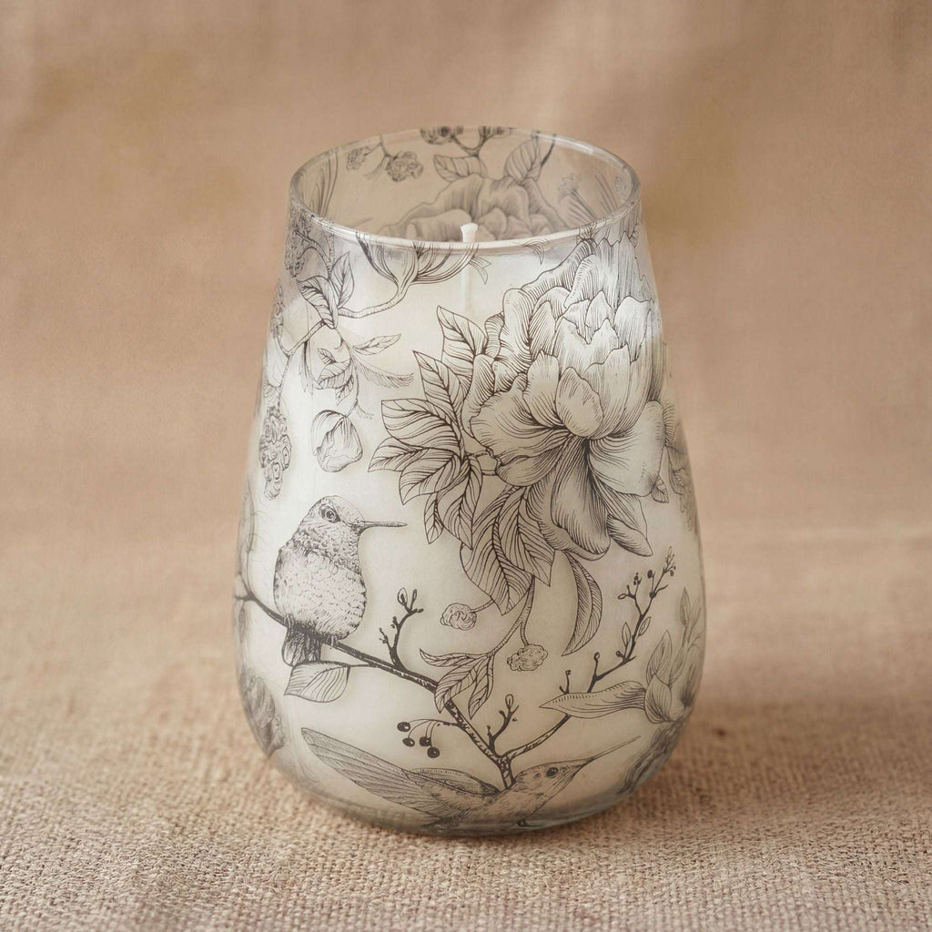 Tall Glass Jar Candles - Drawn by Flame featuring delicate black and white botanical and hummingbird illustrations on a translucent glass jar with a soft beige background.
