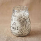 Tall Glass Jar Candles - Drawn by Flame featuring delicate black and white botanical and hummingbird illustrations on a translucent glass jar with a soft beige background.