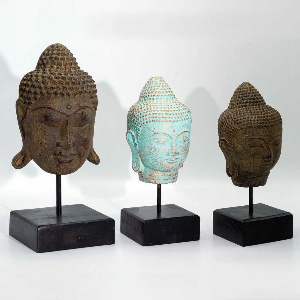 Stillness Buddha Head on Stand - Green Copper displayed alongside two other Buddha heads, each mounted on black square bases, featuring textured details and serene expressions.