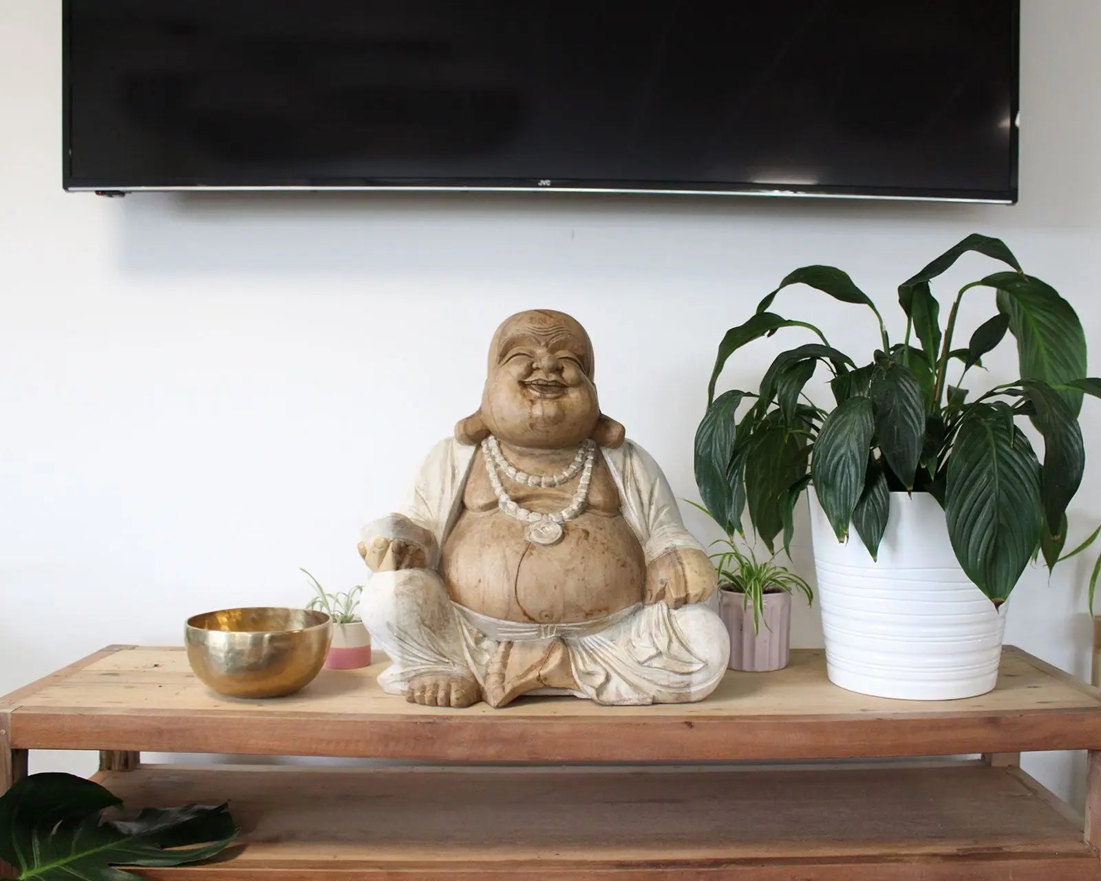 Happy Buddha - Whitewash 50cm sitting on a wooden table beside a brass bowl and potted plants, showcasing hand-carved resin Buddha statue decor.