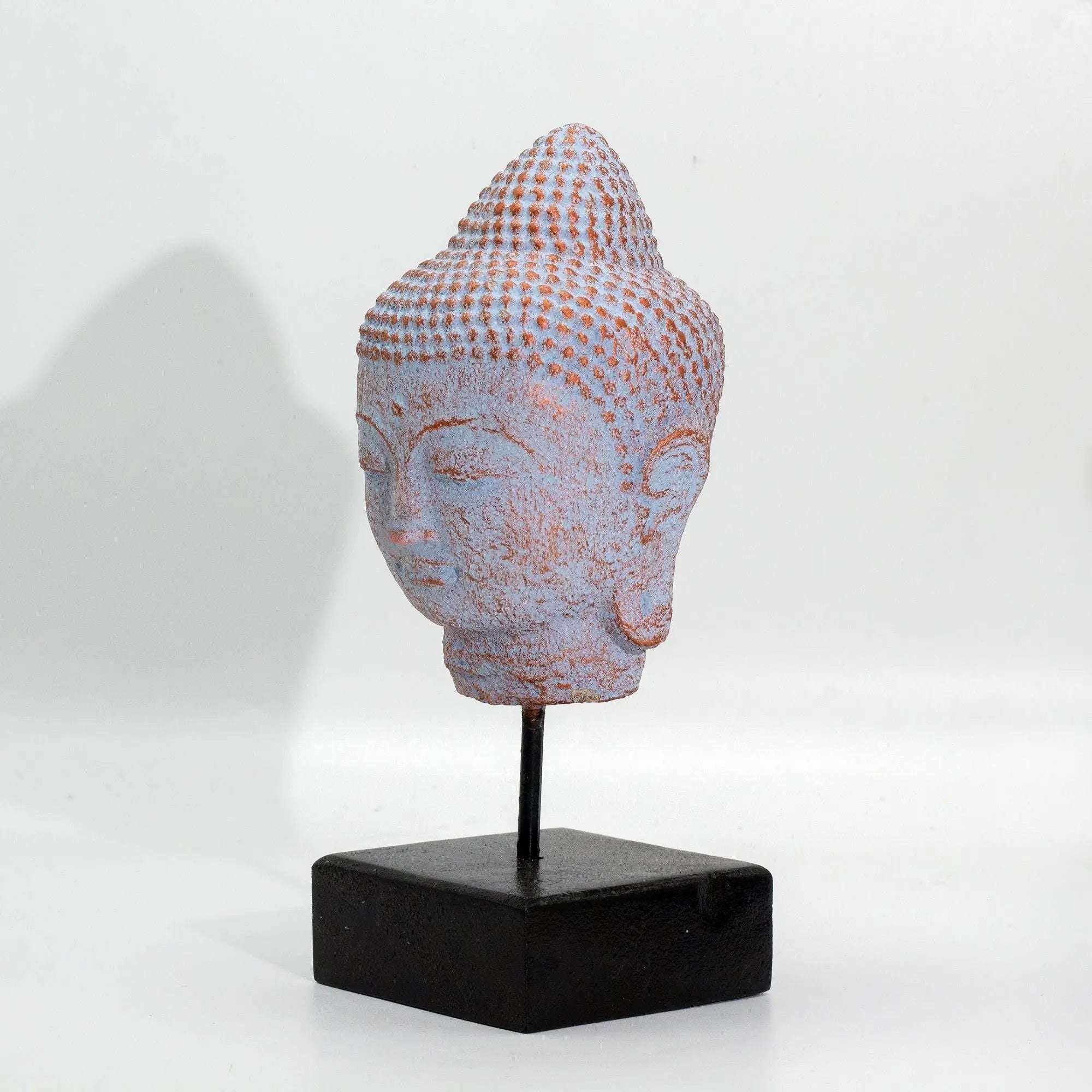 Stillness Buddha Head on Stand - Blue Copper depicts a serene Buddha head sculpture with a textured blue copper finish, mounted on a minimalist black stand, perfect for Buddha decor.